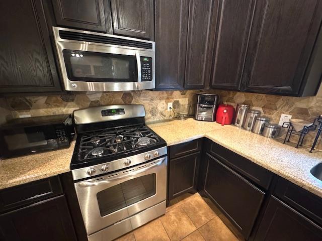 9265 N Sage, Beaumont, TX 77713 - kitchen featuring stainless steel appliances, backsplash, light tile patterned flooring, light stone countertops, and dark brown cabinets