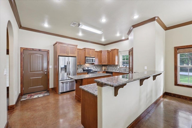 1291 Beachrock Dr, Brookeland, TX 75931 - kitchen with appliances with stainless steel finishes, brown cabinetry, a kitchen bar, concrete floors, and ornamental molding