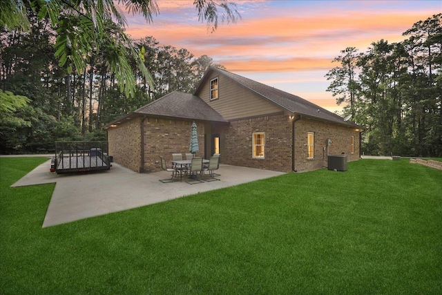 1291 Beachrock Dr, Brookeland, TX 75931 - back of house at dusk featuring a patio, a yard, brick siding, and a shingled roof