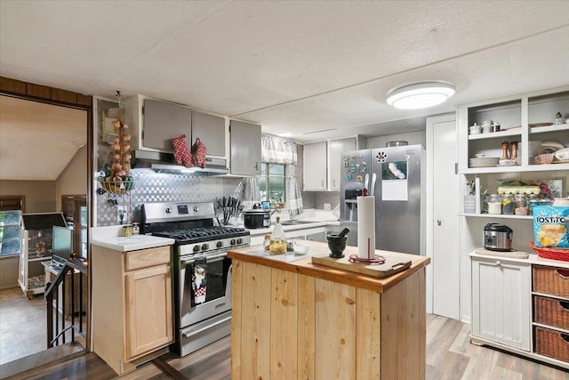 kitchen featuring light wood-type flooring, a textured ceiling, stainless steel appliances, light brown cabinets, and a center island