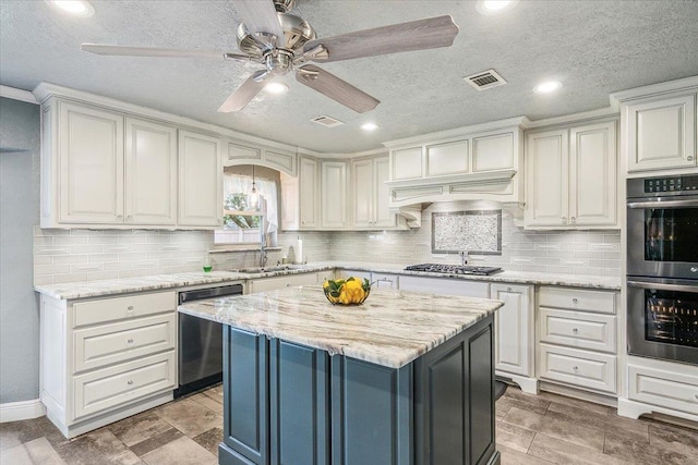 kitchen featuring ceiling fan, sink, a center island, light stone counters, and appliances with stainless steel finishes