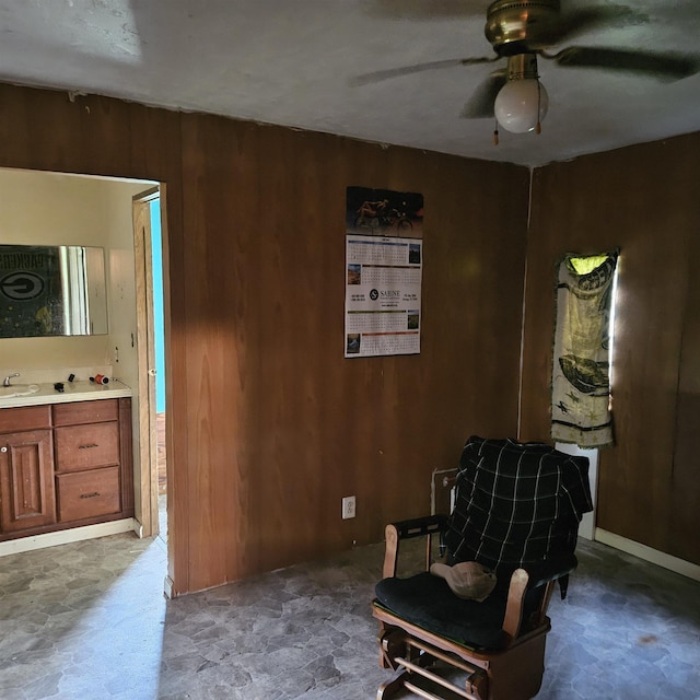 sitting room featuring wood walls, sink, and ceiling fan