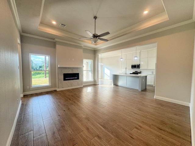 unfurnished living room featuring a high end fireplace, a tray ceiling, a wealth of natural light, and ceiling fan