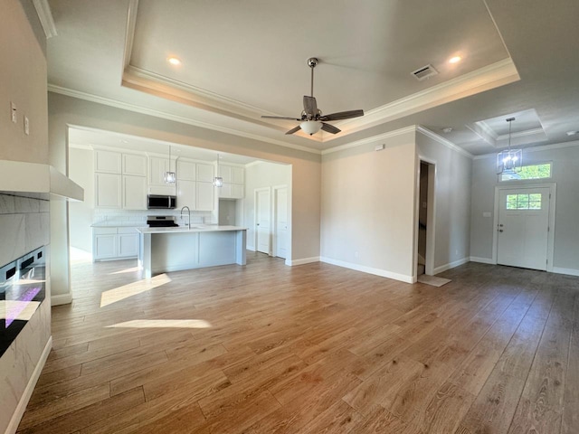 unfurnished living room featuring a tray ceiling, light hardwood / wood-style flooring, ceiling fan, and ornamental molding