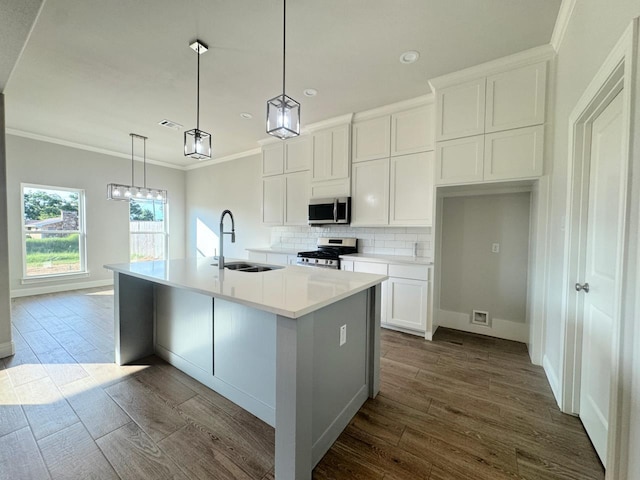 kitchen featuring appliances with stainless steel finishes, a kitchen island with sink, sink, white cabinets, and hanging light fixtures