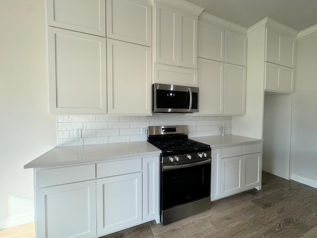 kitchen with appliances with stainless steel finishes, backsplash, dark hardwood / wood-style floors, and white cabinetry