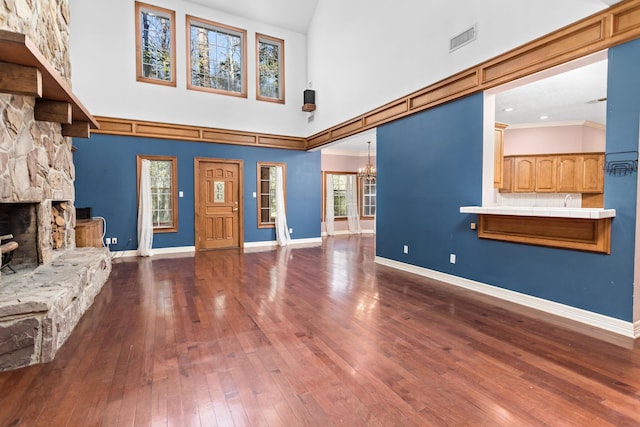 unfurnished living room featuring a stone fireplace, a chandelier, a high ceiling, and hardwood / wood-style flooring