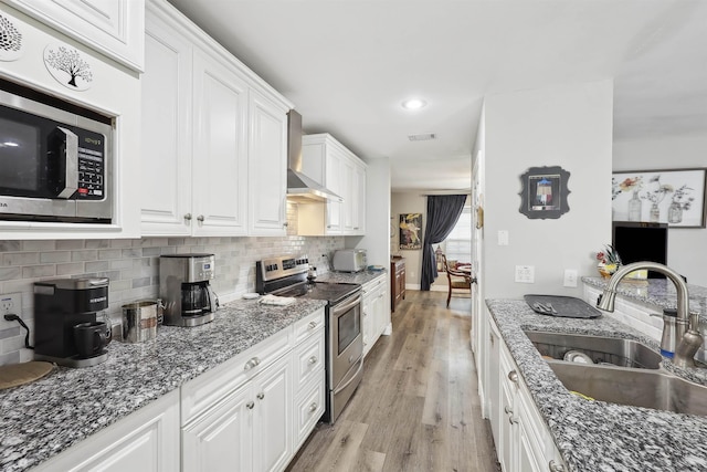 kitchen featuring sink, white cabinetry, stainless steel appliances, dark stone counters, and wall chimney exhaust hood