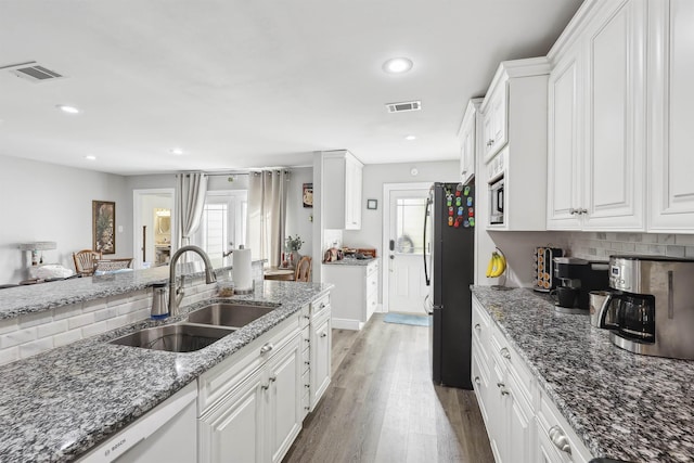 kitchen with sink, white cabinetry, black fridge, dark hardwood / wood-style flooring, and dark stone counters