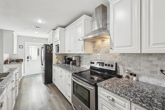 kitchen with white cabinets, stainless steel appliances, dark stone counters, and wall chimney exhaust hood