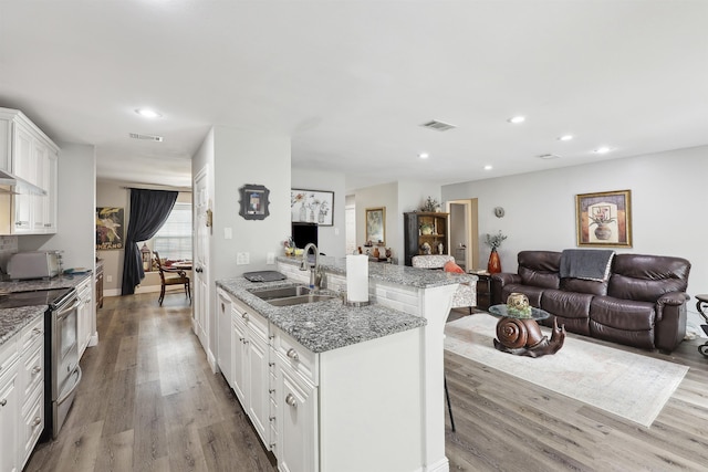 kitchen with sink, dark stone countertops, a kitchen breakfast bar, white cabinets, and stainless steel electric stove