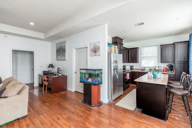 kitchen featuring dark brown cabinetry, a center island, a kitchen breakfast bar, stainless steel refrigerator with ice dispenser, and light hardwood / wood-style floors