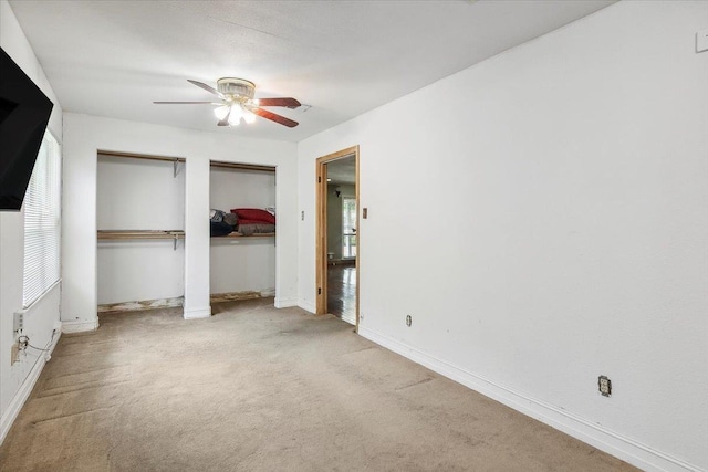 unfurnished bedroom with light carpet, two closets, and ceiling fan