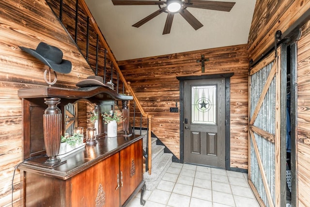 tiled entrance foyer with wooden walls, ceiling fan, and vaulted ceiling