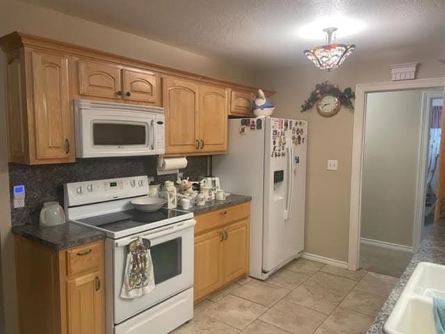 kitchen with a textured ceiling, backsplash, white appliances, and sink