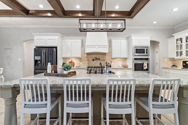 6526 Brayfield Ln, Beaumont, TX 77706 - kitchen with appliances with stainless steel finishes, custom exhaust hood, arched walkways, white cabinets, and backsplash