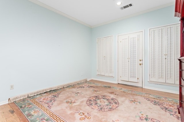 unfurnished bedroom with wood-type flooring, ornamental molding, and multiple closets