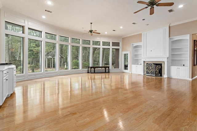 unfurnished living room featuring crown molding, built in features, ceiling fan, and light wood-type flooring