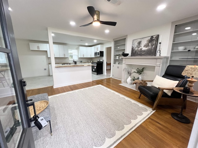 living room with built in shelves, light hardwood / wood-style flooring, and ceiling fan