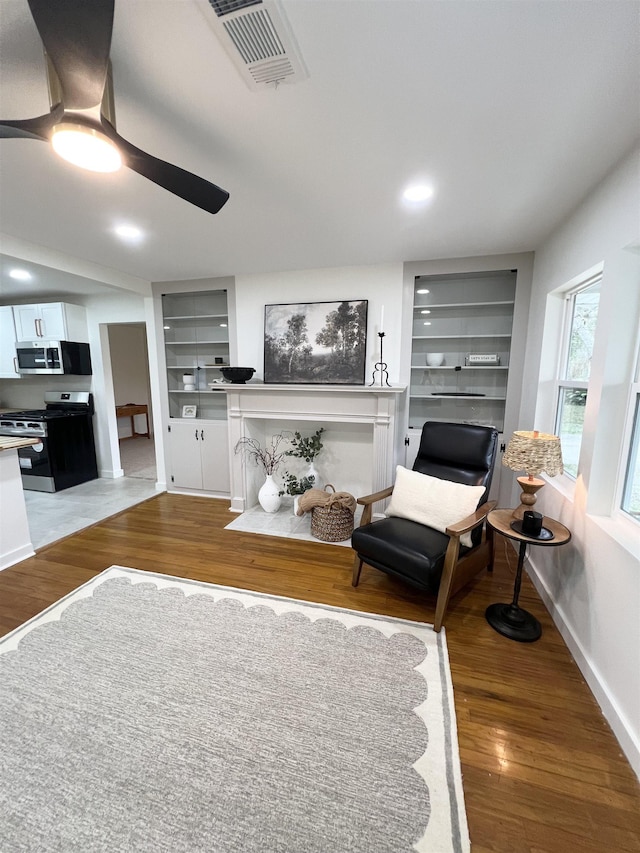 living room featuring hardwood / wood-style floors, built in shelves, and ceiling fan