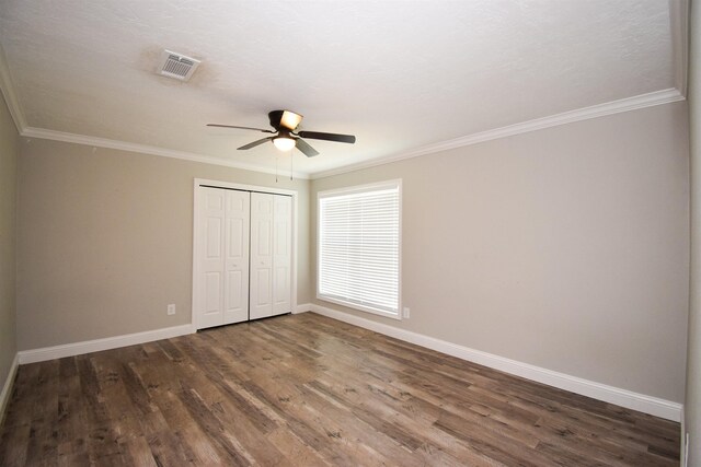 unfurnished bedroom with ceiling fan, a closet, dark wood-type flooring, and crown molding