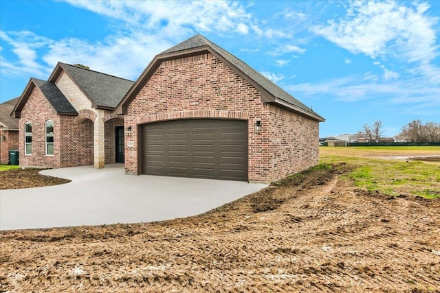 exterior space with brick siding, an attached garage, a shingled roof, and driveway