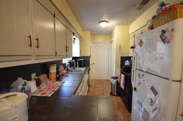 kitchen with tile countertops, white refrigerator, sink, a textured ceiling, and light tile patterned flooring