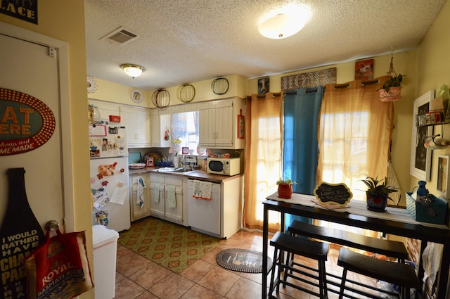 kitchen with white cabinetry, white appliances, a textured ceiling, and light tile patterned floors