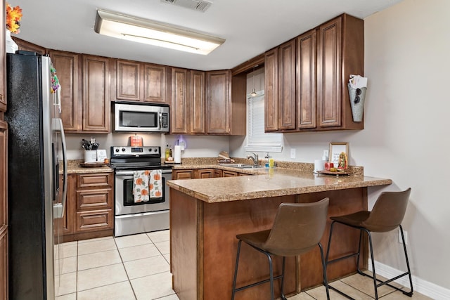 kitchen featuring kitchen peninsula, a kitchen breakfast bar, stainless steel appliances, sink, and light tile patterned floors