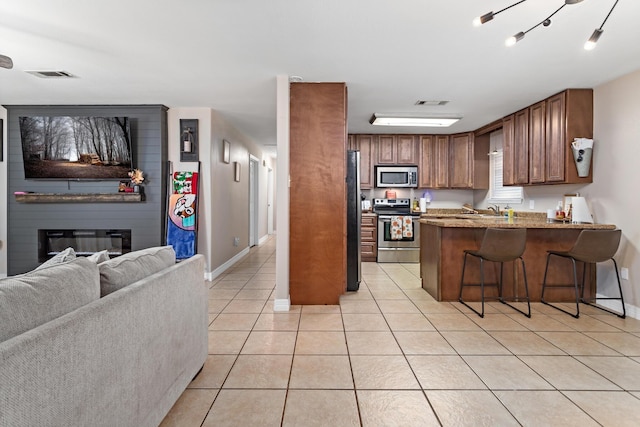 kitchen featuring a large fireplace, stainless steel appliances, a kitchen breakfast bar, kitchen peninsula, and light tile patterned floors