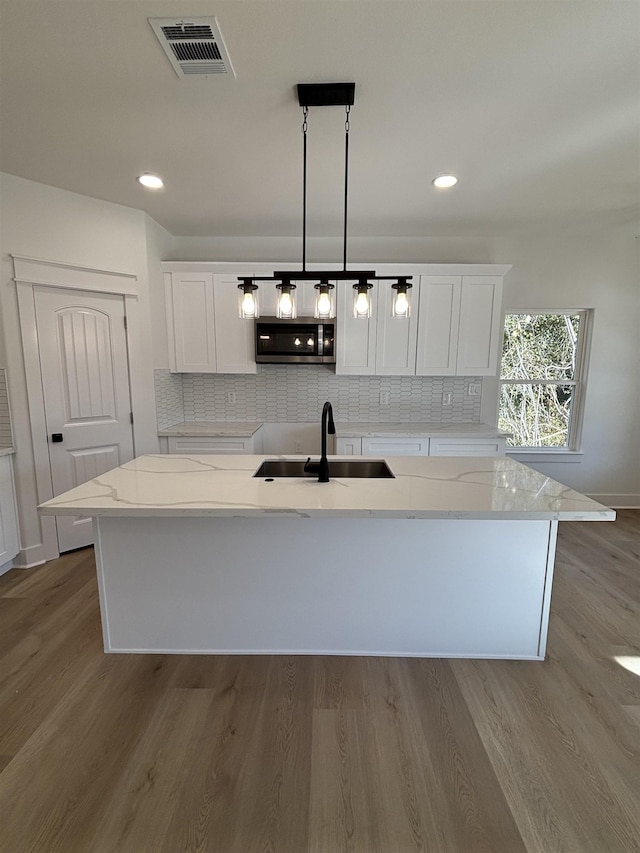 kitchen with sink, white cabinetry, pendant lighting, and an island with sink