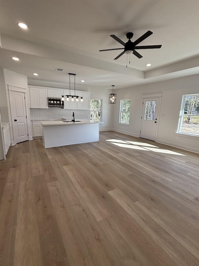 unfurnished living room featuring ceiling fan with notable chandelier, light hardwood / wood-style floors, and sink