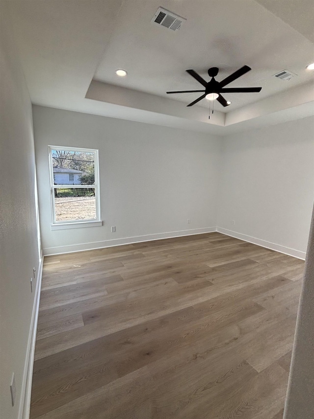 empty room with hardwood / wood-style flooring, ceiling fan, and a tray ceiling