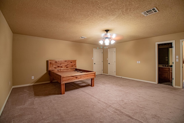 carpeted bedroom featuring a textured ceiling, ensuite bath, and ceiling fan