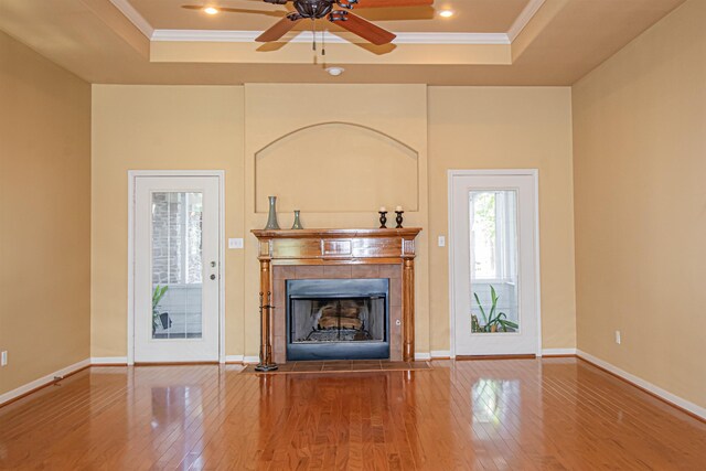 unfurnished living room featuring a tray ceiling, crown molding, a fireplace, and hardwood / wood-style flooring