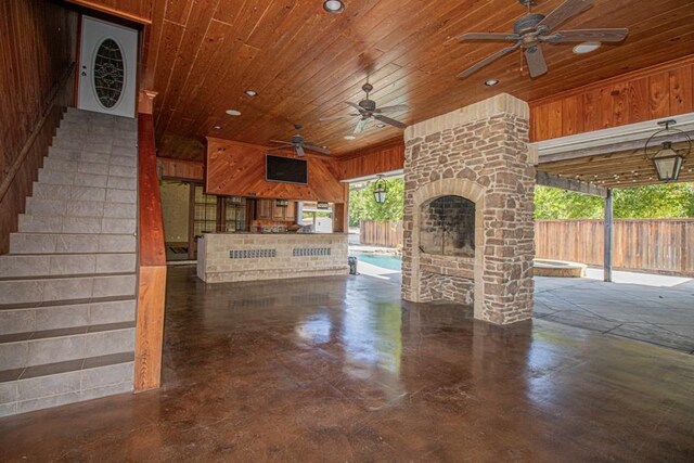 unfurnished living room with an outdoor stone fireplace, wood walls, wood ceiling, and ceiling fan