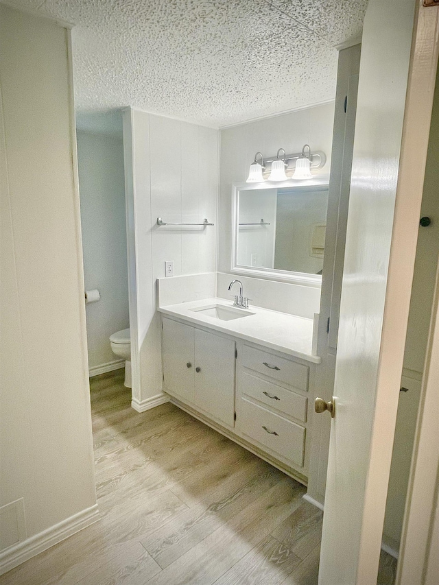 bathroom with toilet, a textured ceiling, wood finished floors, baseboards, and vanity