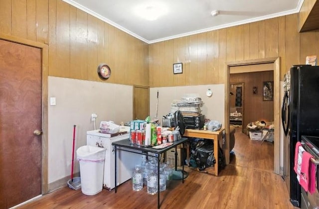 kitchen featuring black fridge, wood walls, hardwood / wood-style flooring, and ornamental molding