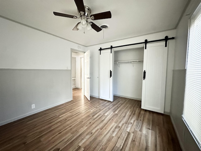312 Temple, Woodville, TX 75979 - unfurnished bedroom with wood finished floors, a barn door, a closet, and ceiling fan