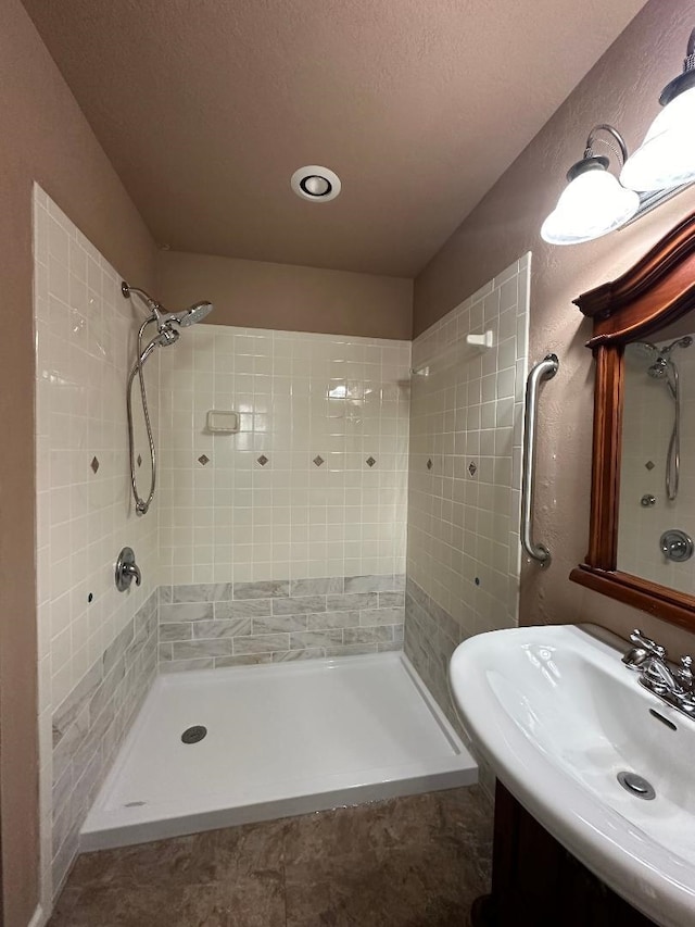 bathroom with a tile shower, vanity, and a textured ceiling