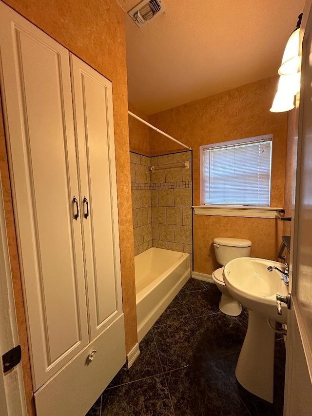 bathroom with tile patterned flooring, toilet, and tiled shower / bath