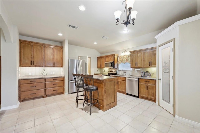 7385 Hidden Valley Dr, Beaumont, TX 77706 - kitchen featuring appliances with stainless steel finishes, tasteful backsplash, brown cabinets, a center island, and vaulted ceiling