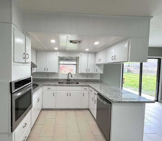 kitchen featuring visible vents, light stone counters, a peninsula, stainless steel appliances, and a sink