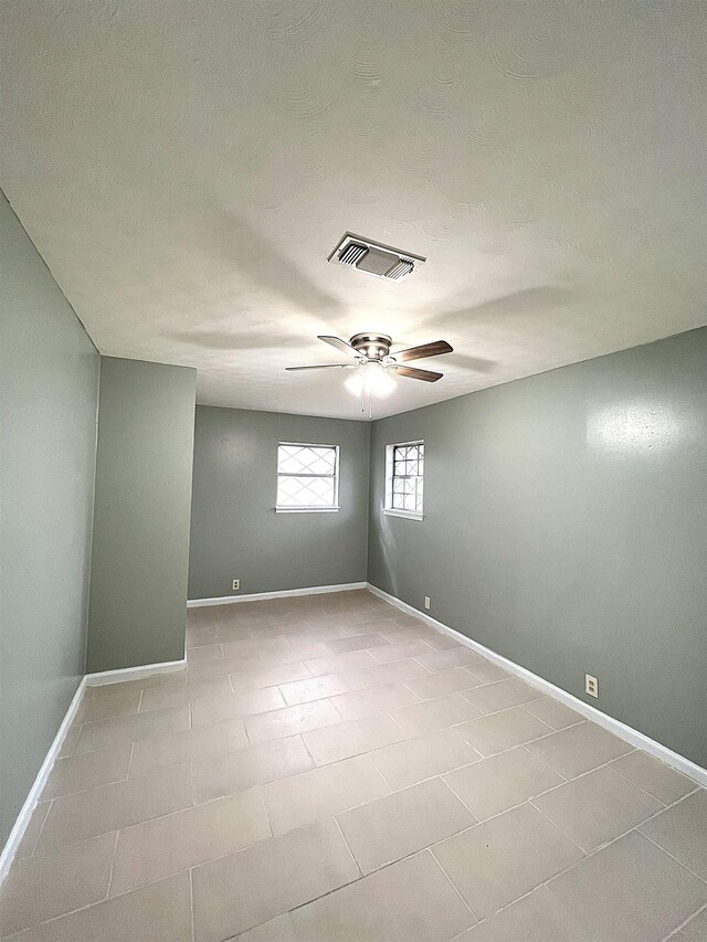 unfurnished room with light tile patterned floors, visible vents, baseboards, and a ceiling fan