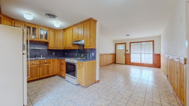 kitchen featuring backsplash, wooden walls, sink, and white appliances