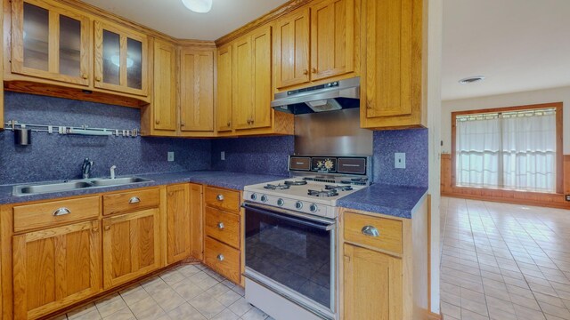 kitchen featuring backsplash, white range with gas stovetop, sink, and light tile patterned floors