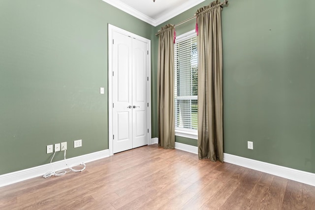 unfurnished bedroom with a closet, crown molding, multiple windows, and light hardwood / wood-style floors