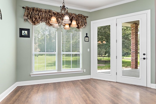 unfurnished dining area with crown molding, wood-type flooring, a wealth of natural light, and an inviting chandelier