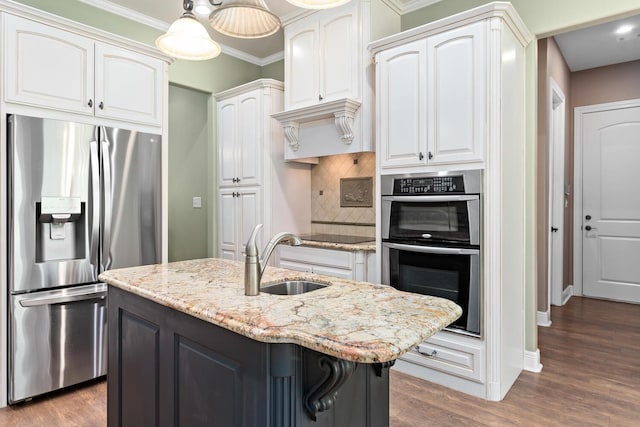 kitchen with decorative light fixtures, white cabinetry, stainless steel appliances, sink, and a center island with sink