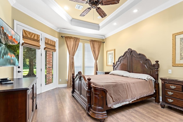 bedroom with hardwood / wood-style flooring, access to outside, ceiling fan, a tray ceiling, and crown molding